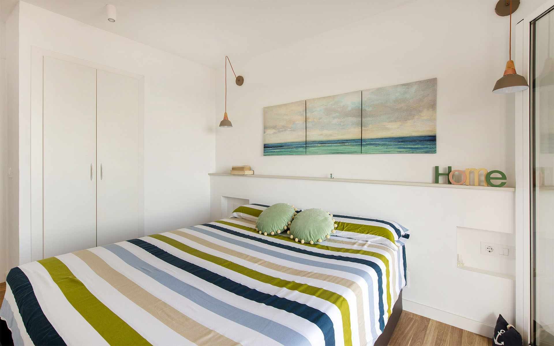 Un dormitorio con una colcha a rayas, un cuadro de un paisaje y una estantería con la palabra 'Home'.