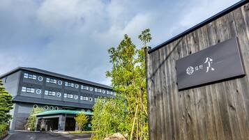 A modern building with a signboard, a parking area, and surrounding greenery.