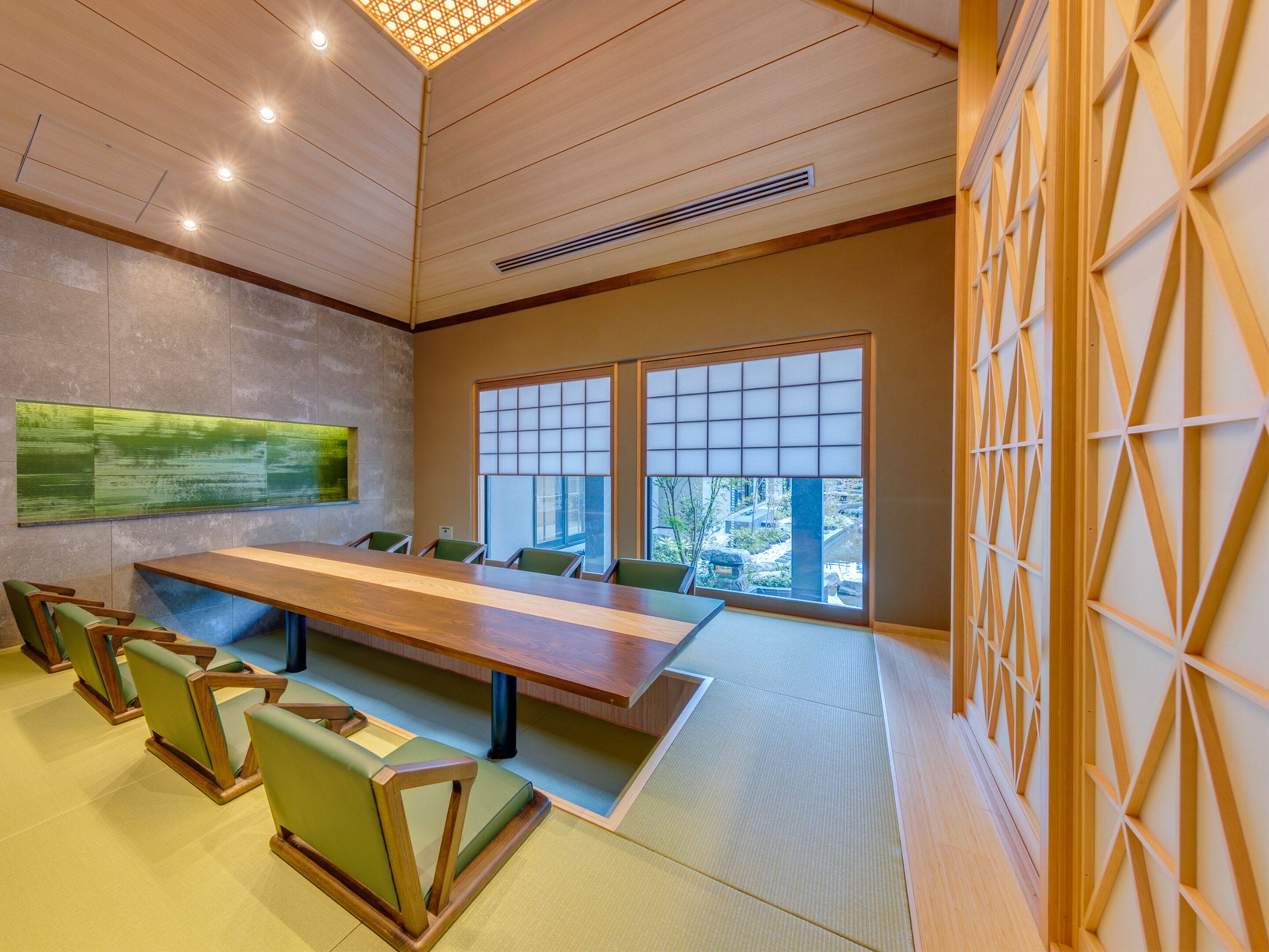 A conference room with a long table, green chairs, large windows, and a wooden ceiling.