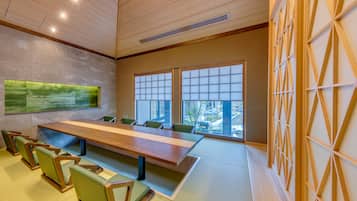A conference room with a long table, green chairs, large windows, and a wooden ceiling.