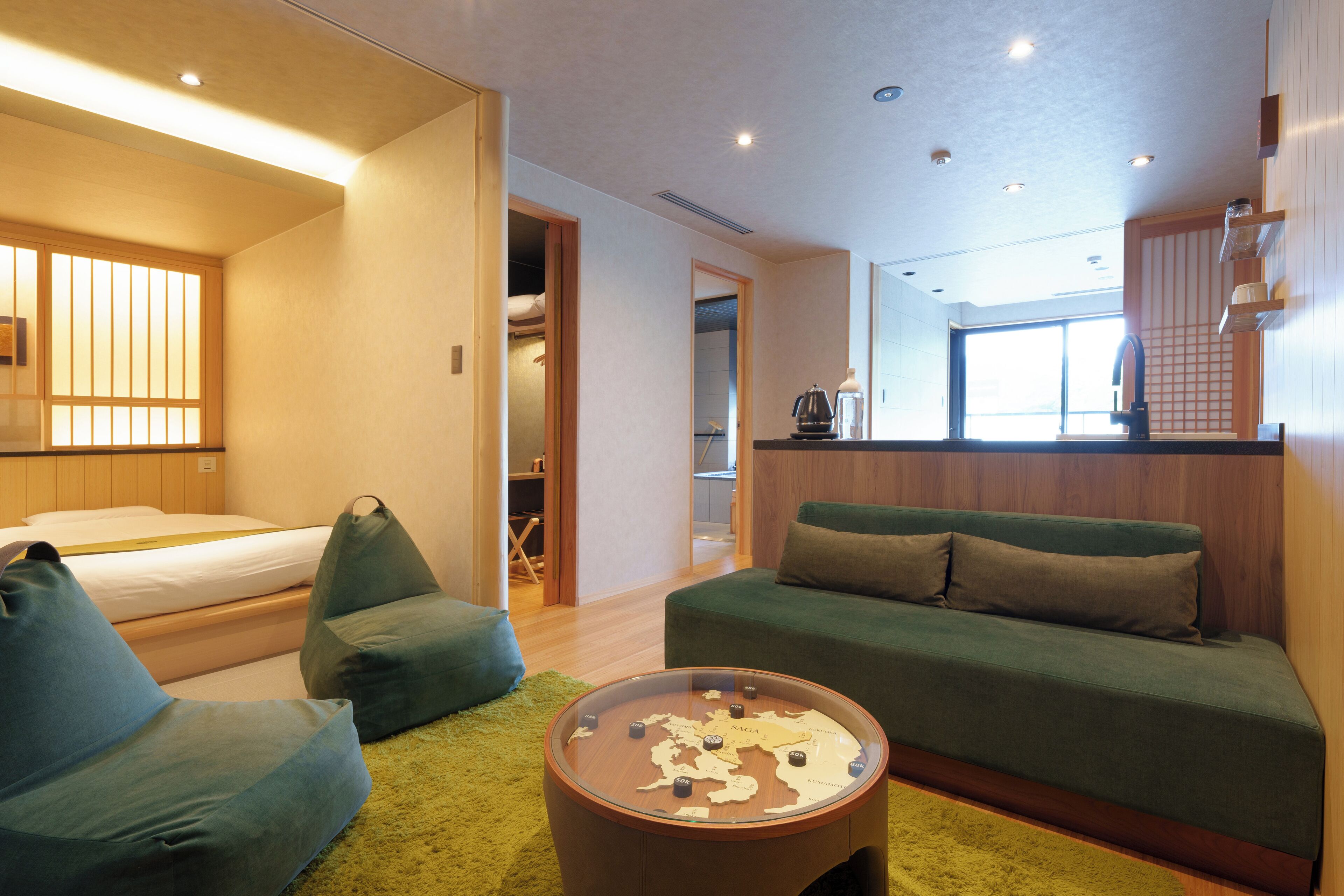 A modern hotel room with a bed, green seating area, and a round coffee table with a map.