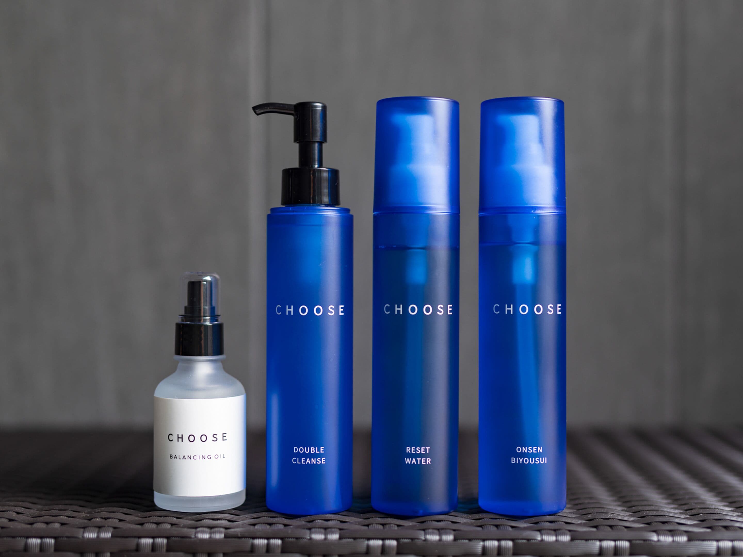 Quatre bouteilles de produits de soins pour la peau, portant la marque « CHOOSE », sont posées sur une surface tissée.