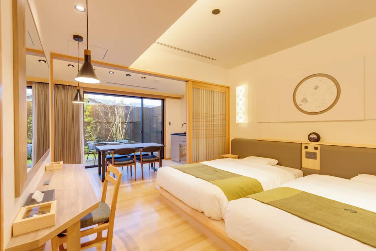 A hotel room with two beds, a desk, and a dining area with a table and chairs.