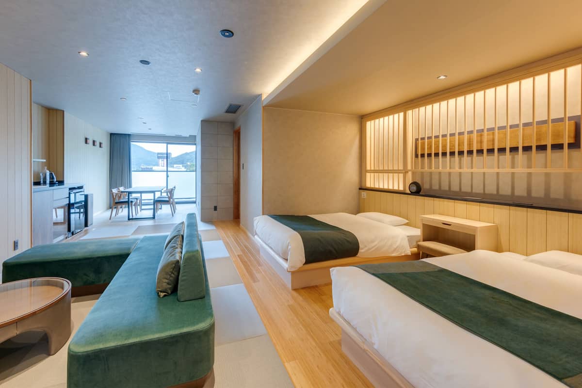 A modern hotel room with two beds, a dining area, and a view of the sea.