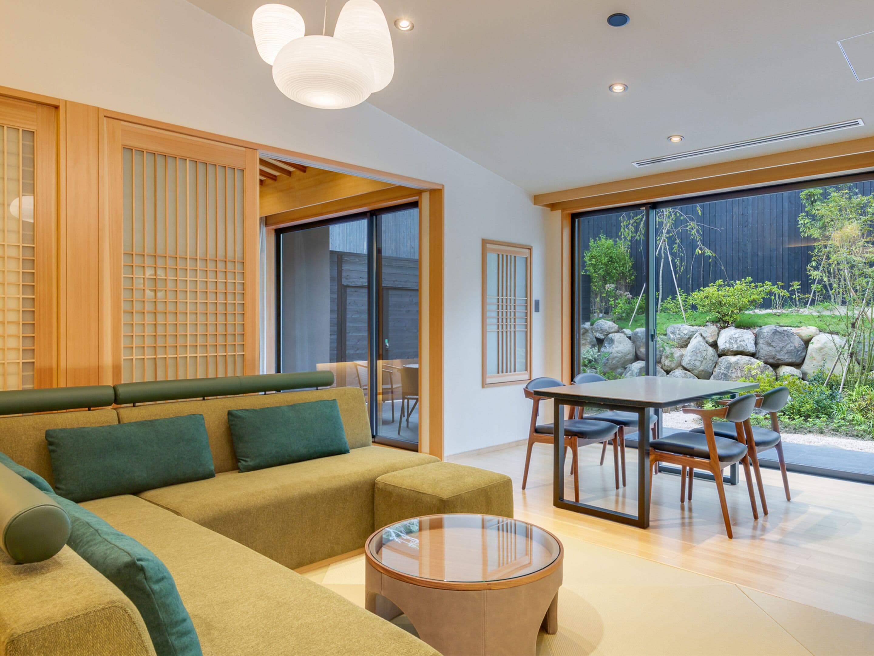 A modern living room with a sofa, a glass coffee table, and a dining area with a table and chairs.