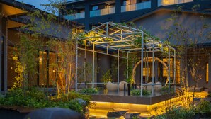 Un jardín moderno al aire libre con una estructura de vidrio, asientos y fuentes de agua.