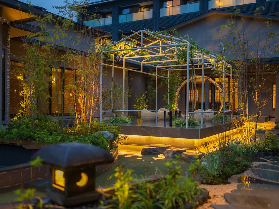 A modern outdoor garden with a glass structure, seating, and water features.