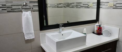 Un baño con un lavamanos blanco, un espejo, un aro para toallas y un dispensador de jabón.
