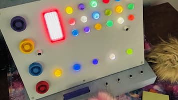A control panel with a red light, various buttons, and a hammer on a desk with a galaxy-themed tablecloth.
