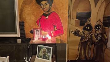 A room with a mural, a framed photo, candles, and a small table with flowers.