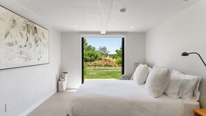 Un dormitorio moderno con una cama grande, vista a un jardín a través de una puerta abierta y un cuadro en la pared.