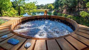 Un jacuzzi con cubierta de madera, rodeado de un paisaje natural y una extensión de agua.