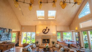 Una sala de estar amplia con chimenea, ventiladores de techo y ventanas grandes.