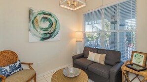 Un salon avec un canapé gris, un fauteuil en osier, une table basse ronde et un grand tableau abstrait accroché au mur.