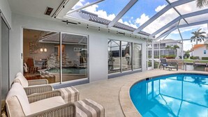 Een zwembadterras met een glazen patio, rieten meubels en uitzicht op het zwembad.