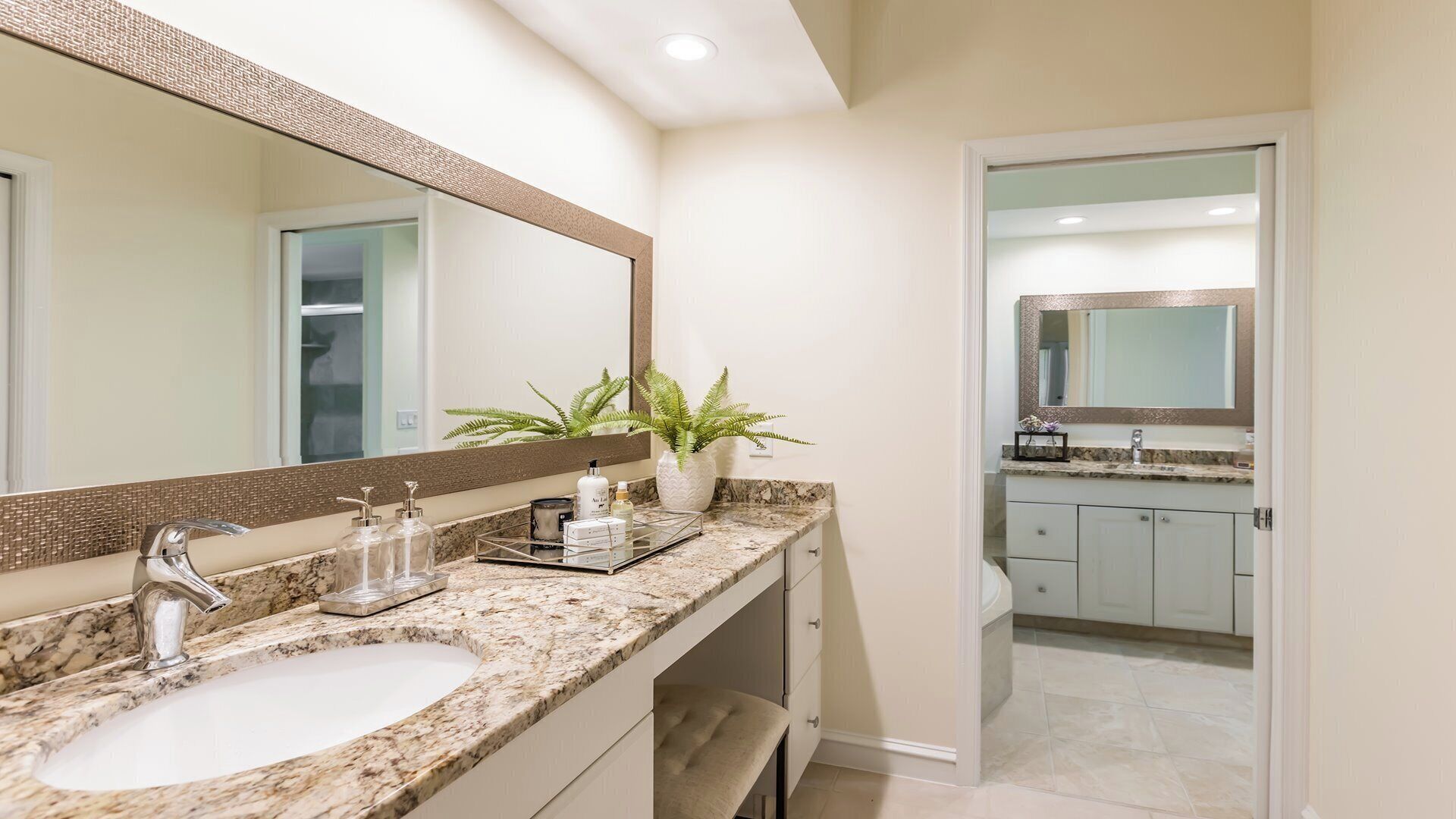 A modern bathroom with a large mirror, granite countertop, and a potted plant.
