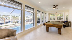 A pool area with a pool table, a chair, and large windows overlooking a pool and a marina. - 3/2 Waterfront Pool/Spa Home (Marco Island)