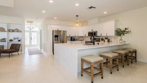 A modern kitchen with white cabinetry, a central island with stools, stainless steel appliances, and a pendant light. - 3/2 Waterfront Pool/Spa Home (Marco Island)