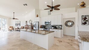 Una cocina amplia con una isla grande, muebles blancos y electrodomésticos modernos.