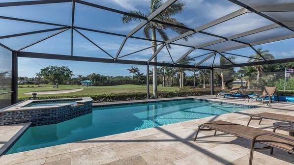 A pool area with a view of a golf course, covered patio, and lounge chairs.