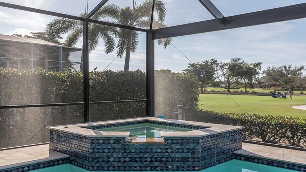 Un jacuzzi con diseño de mosaicos, rodeado por un recinto de vidrio, con vista a un campo de golf.