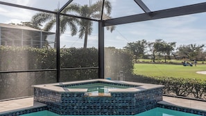 A hot tub with mosaic tile design, surrounded by a glass enclosure, overlooking a golf course.