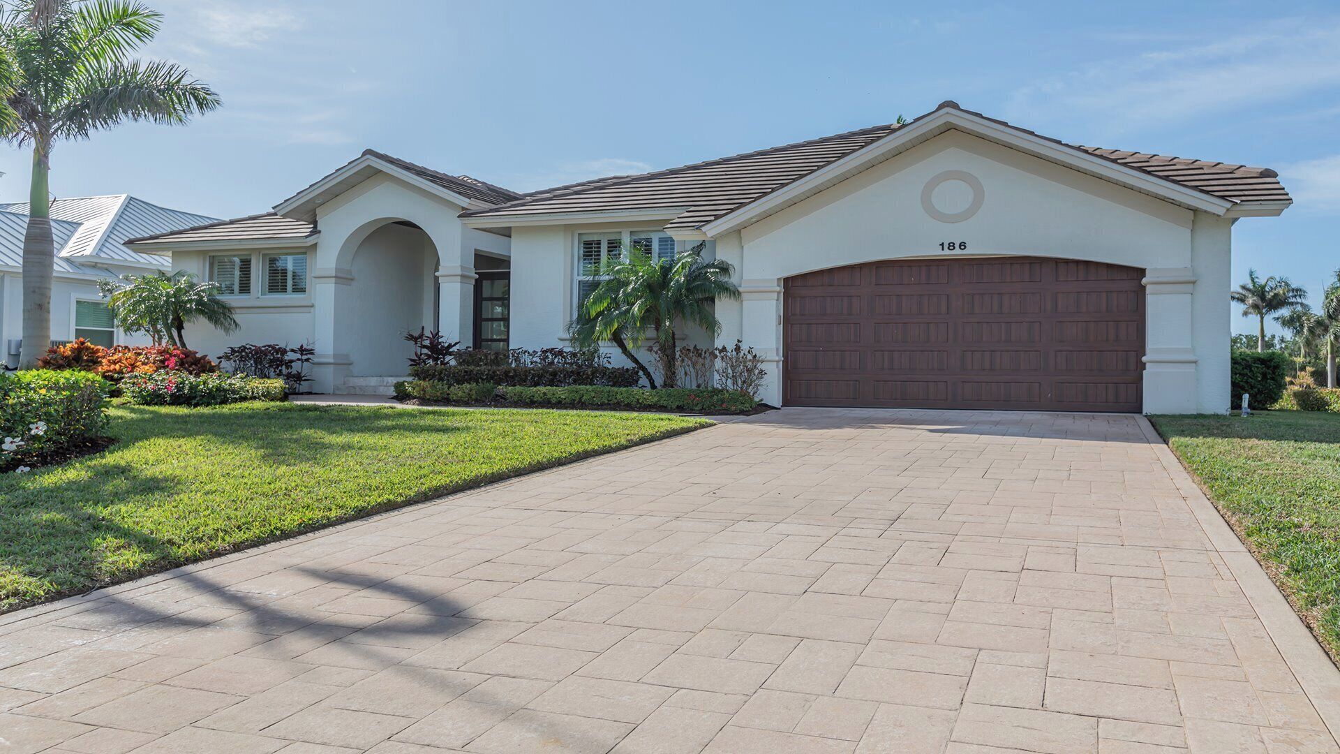 A two-story house with a driveway leading to a garage, surrounded by well-maintained landscaping and palm trees.