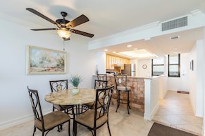 A dining area with a round table, six chairs, a ceiling fan, and a painting on the wall.