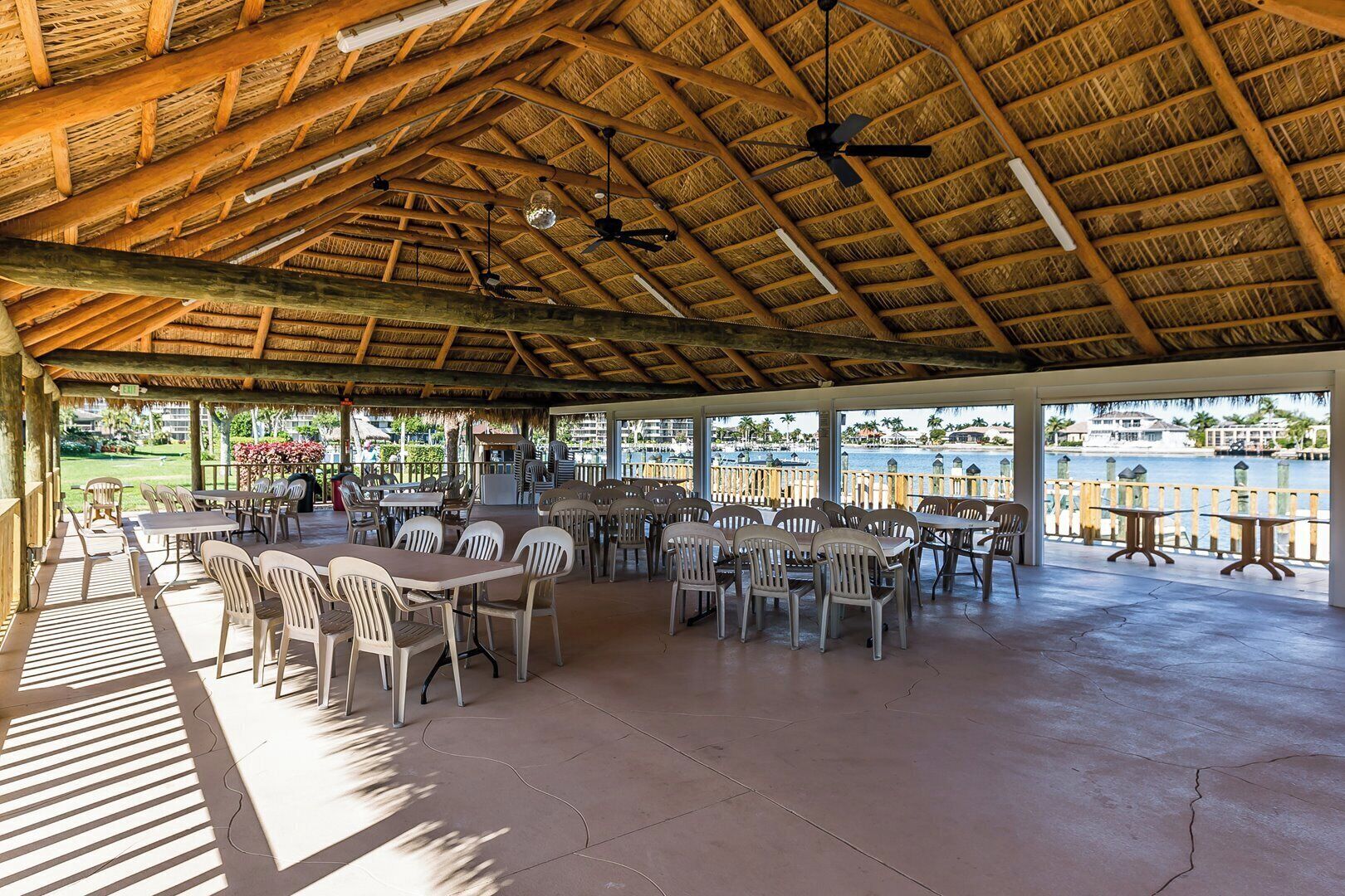 Une terrasse extérieure avec des tables et des chaises, un toit de chaume et une vue sur l’eau.