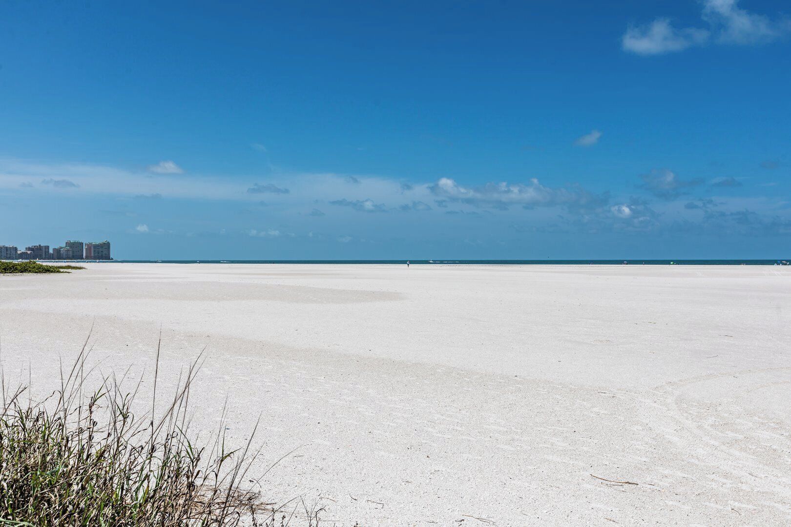 En bred, åben sandstrand med en klar blå himmel og bygninger i det fjerne.