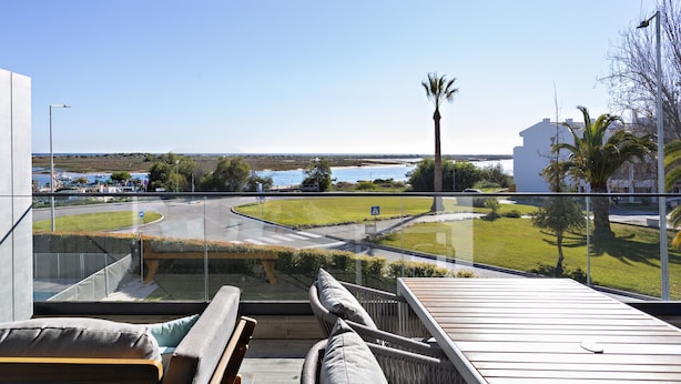 Un balcone con vista su una strada, palme e un corpo d'acqua.