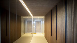Un corridoio moderno con pannelli in legno, porte in vetro e una lampada a soffitto luminosa.