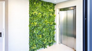 Un ascensore moderno con finiture metalliche e una parete decorata con un giardino verticale.