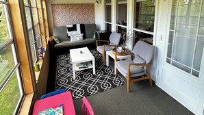 Ein überdachter Balkon mit Holzboden, einer Couch, zwei Stühlen, einem kleinen Tisch und Blick ins Grüne.