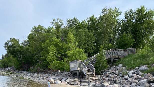 Ein Strand mit einer Holztreppe, die zu einer Plattform führt, umgeben von Felsen und Bäumen.
