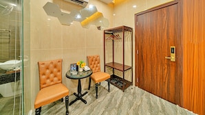 A bathroom with a glass shower enclosure, two brown leather chairs, a small round table with toiletries, and a wooden wardrobe. - S79 T68 Hotel Go Vap (Ho Chi Minh City)
