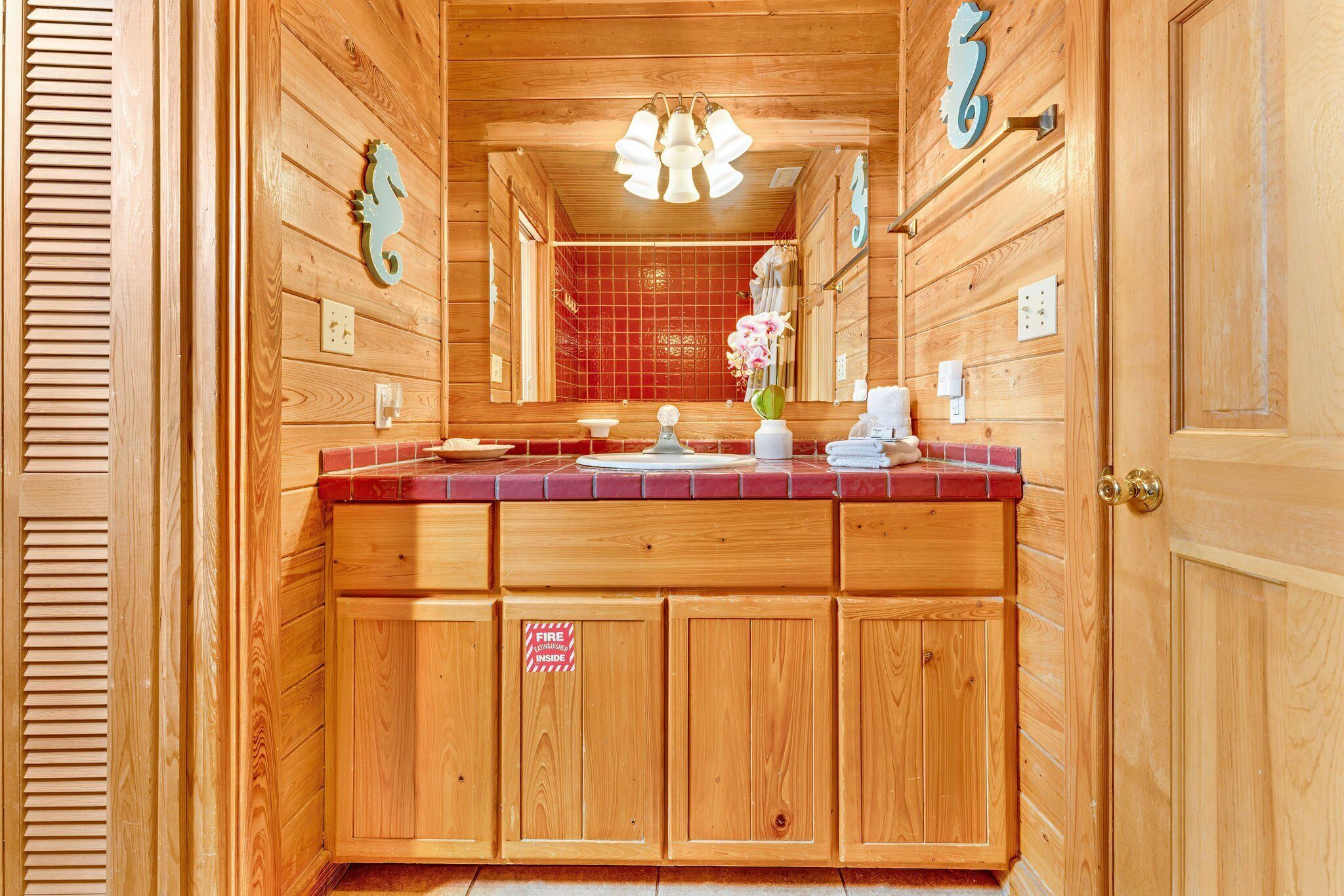 Un baño de madera con ducha de azulejos rojos, tocador de madera y un espejo.