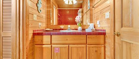 Un baño de madera con ducha de azulejos rojos, tocador de madera y un espejo.