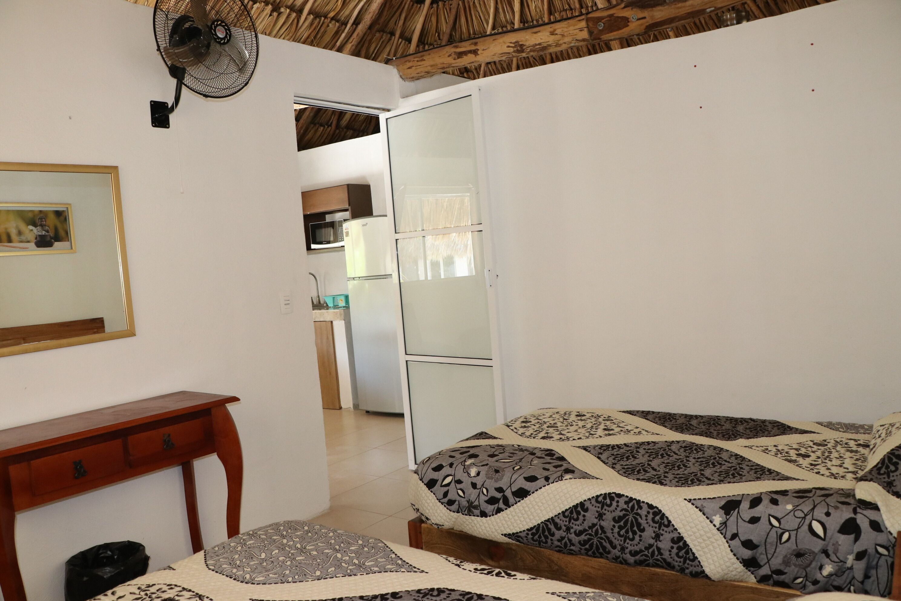 A bedroom with a bed, a wooden nightstand, a desk, and a fan.