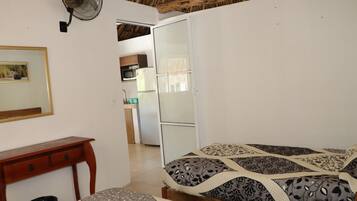 A bedroom with a bed, a wooden nightstand, a desk, and a fan.