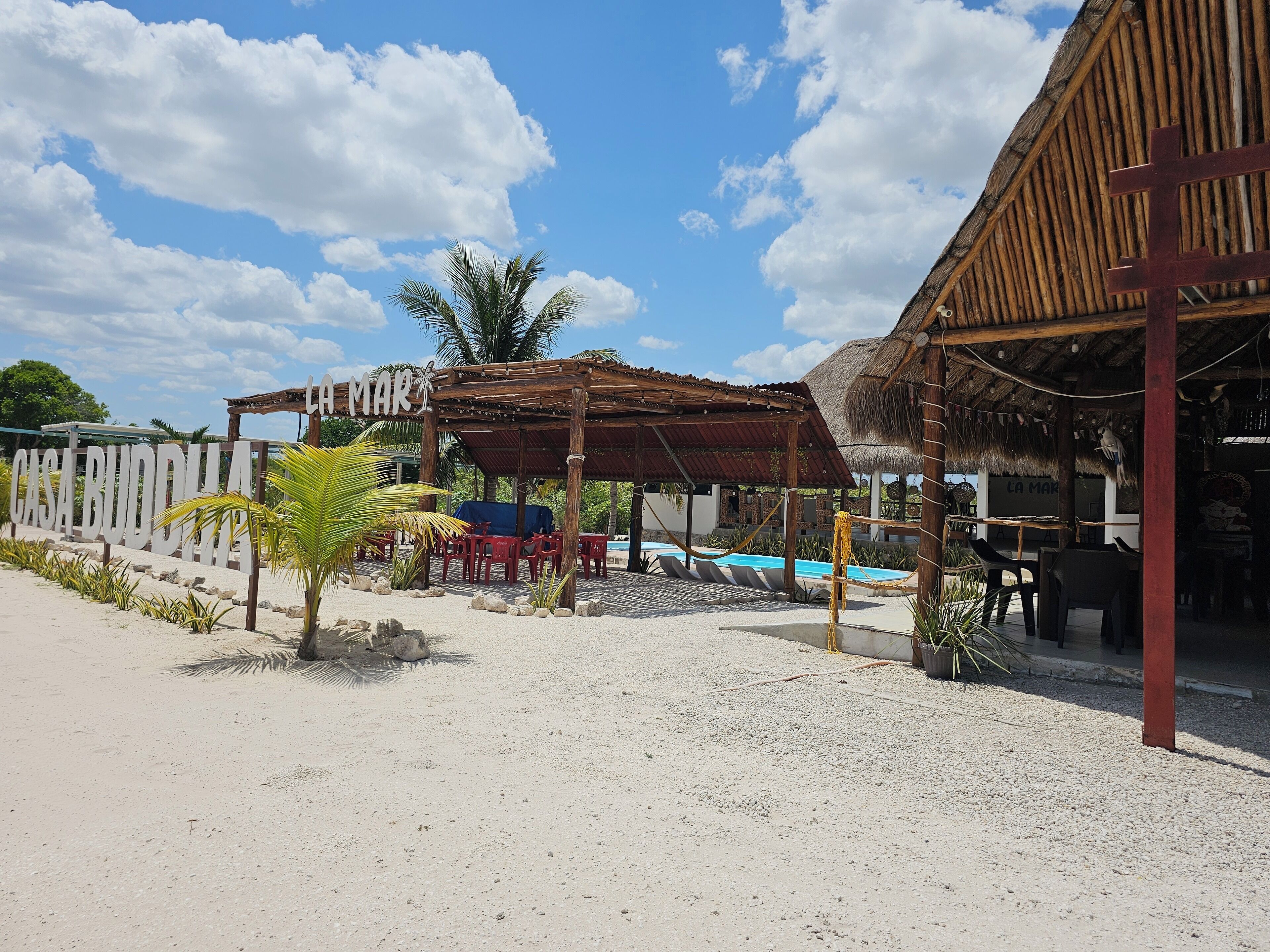 Un resort frente a la playa con piscina, mobiliario exterior y una estructura de techo de paja.
