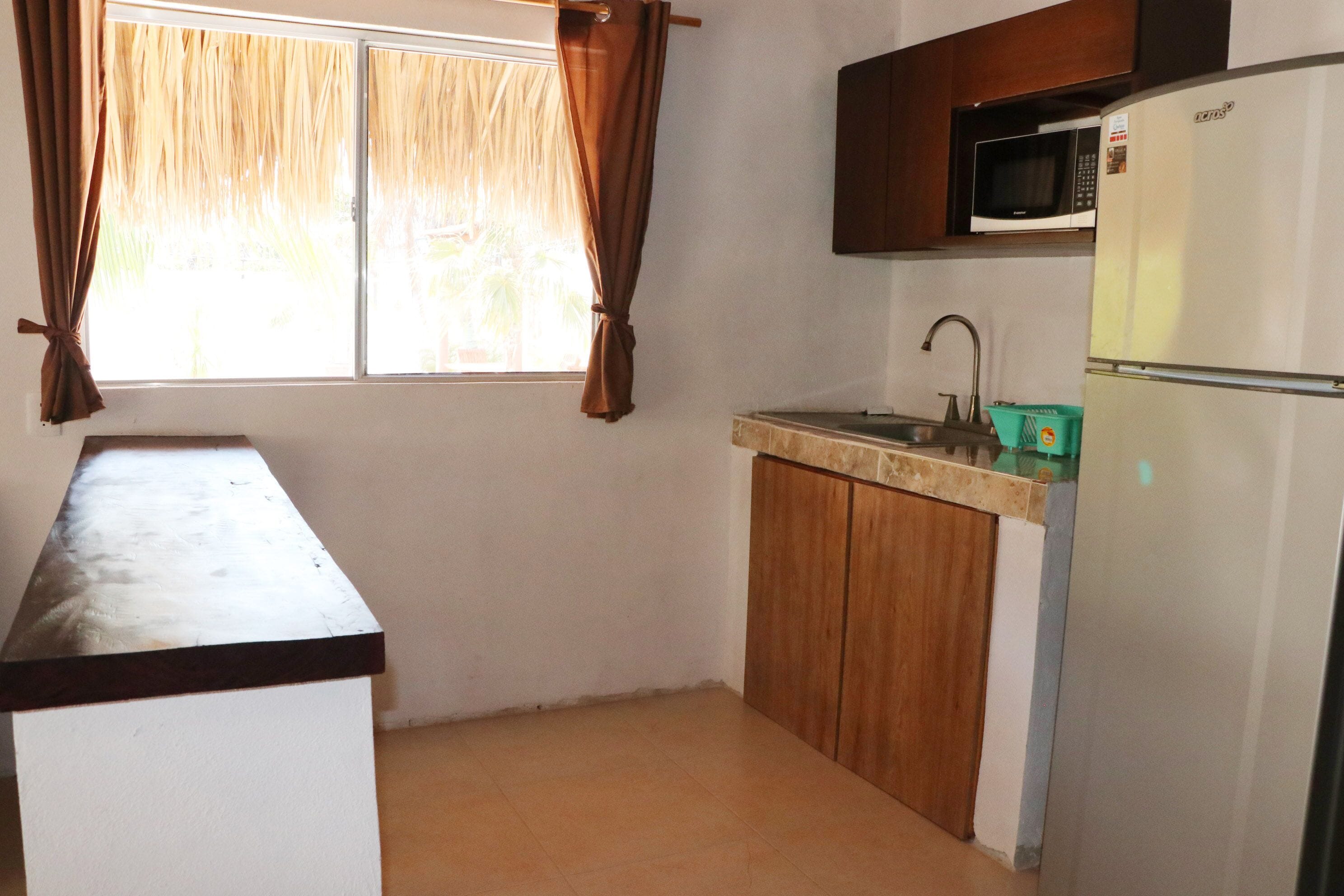 A small kitchen with a refrigerator, a microwave, a sink, and wooden cabinets.