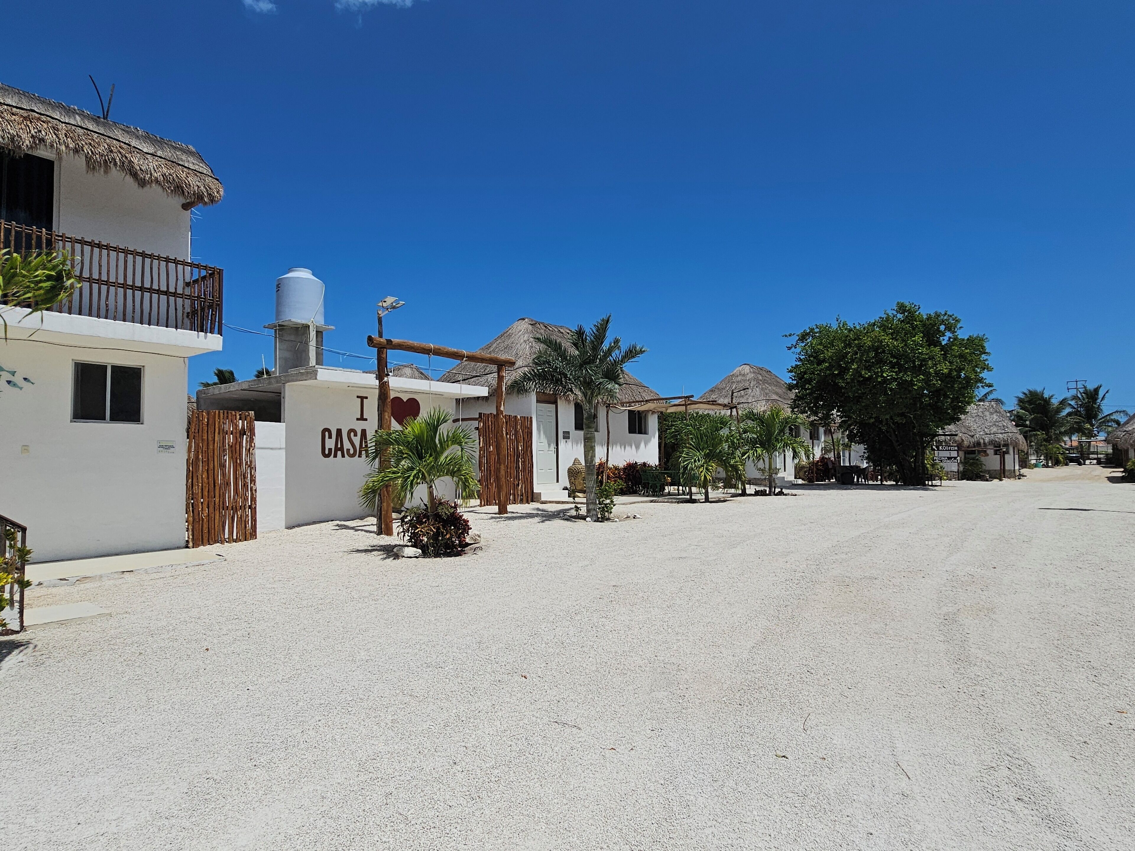 A coastal village with white buildings, palm trees, and thatched-roof structures.