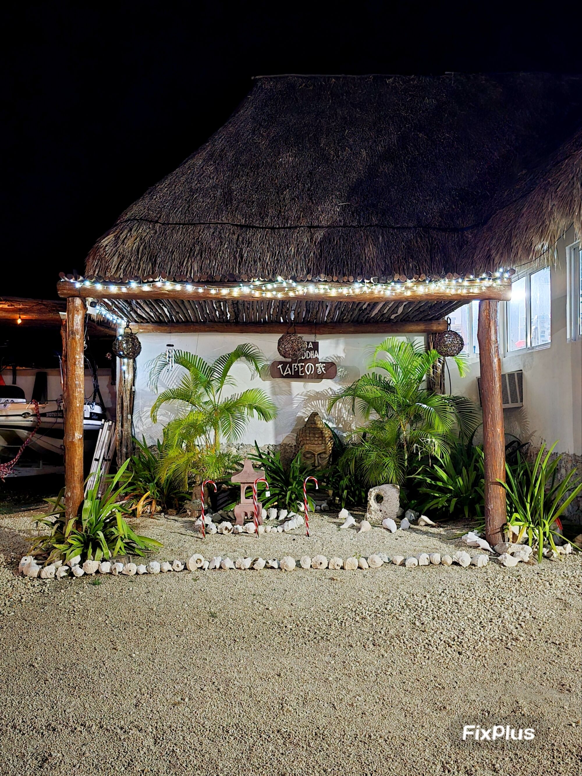 A thatched-roof structure with a sign reading "Aloha TAFELO'S" surrounded by tropical plants and a gravel path.