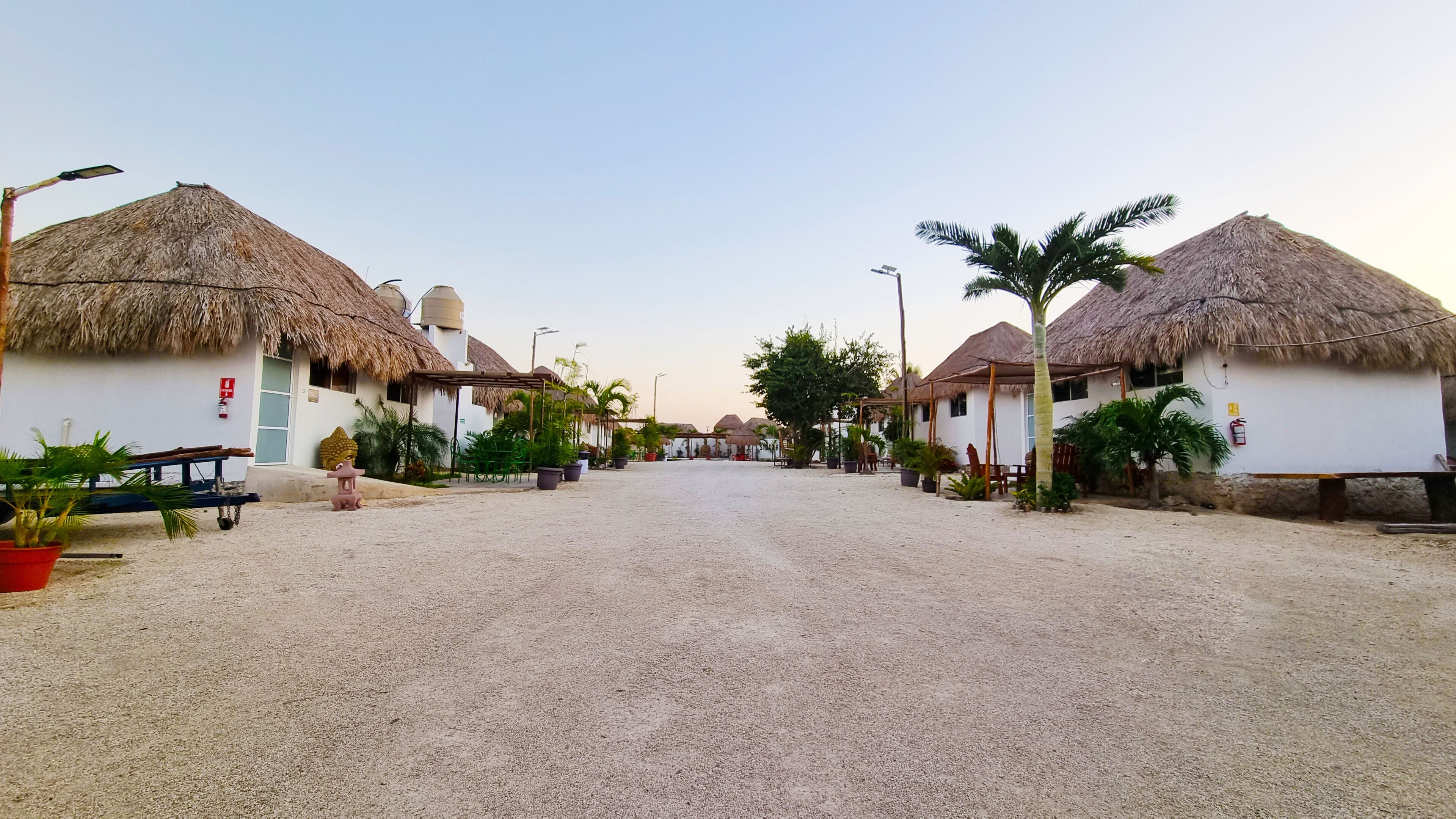 A street lined with thatched-roof houses, a gravel road, and potted plants.