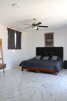 A bedroom with a bed, a ceiling fan, a painting, and a wooden easel.