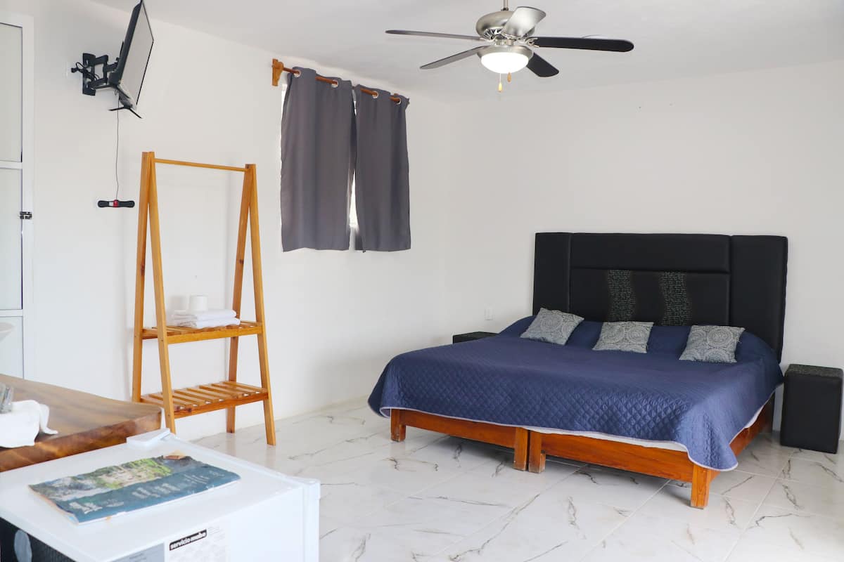 A bedroom with a bed, a wooden shelf, a ceiling fan, and a window with curtains.