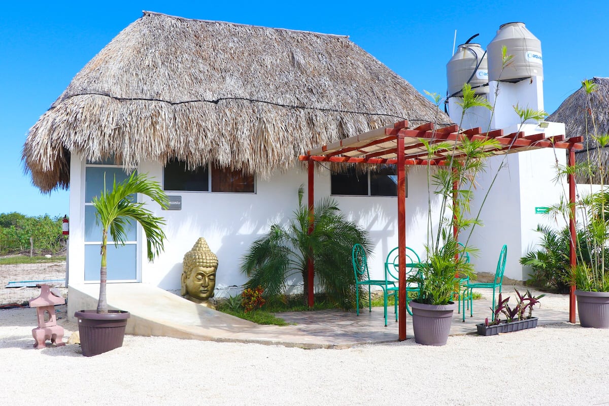 A thatched-roof building with a white exterior, a Buddha statue, and a pergola with chairs.
