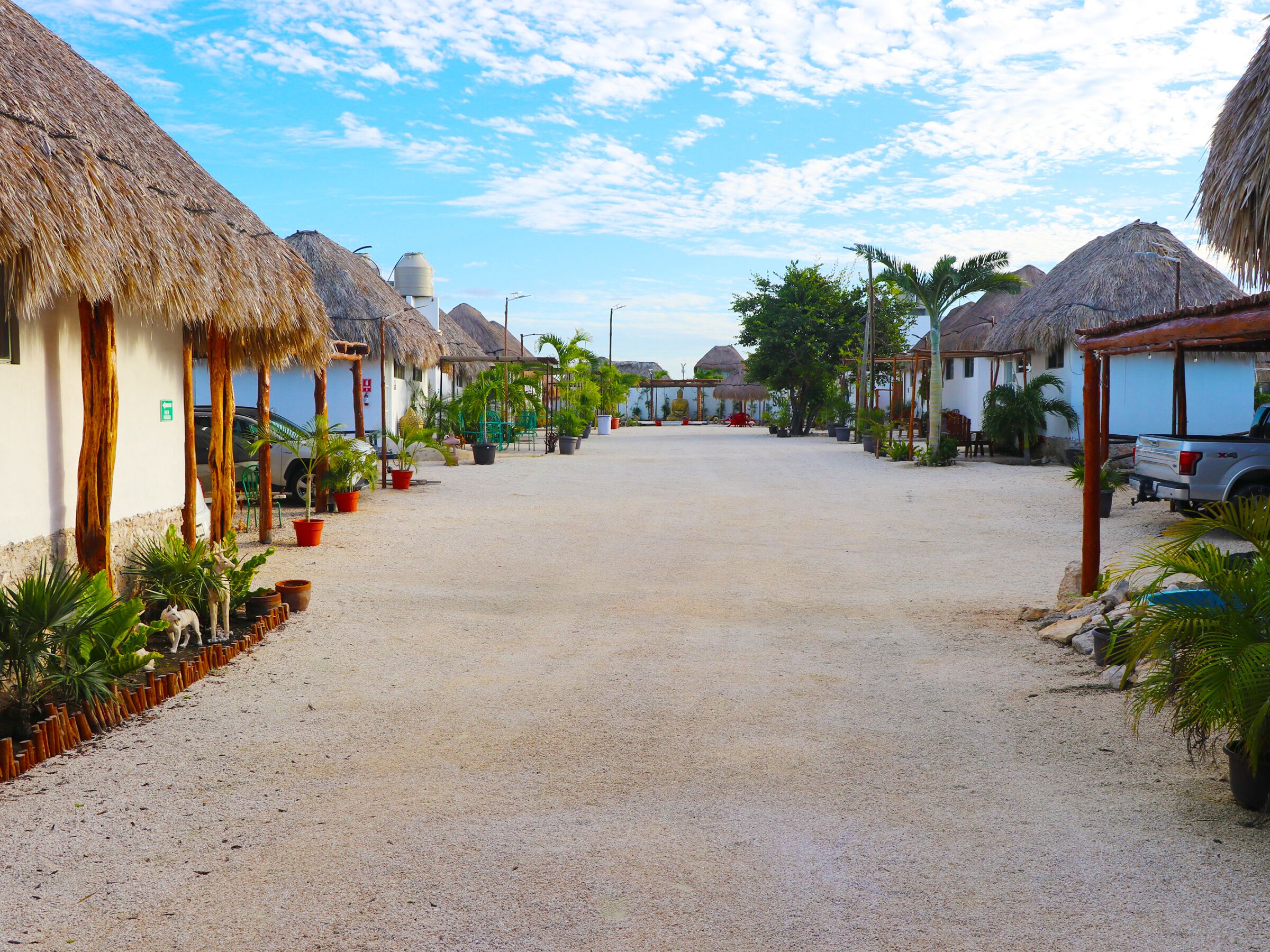 A street lined with thatched-roof houses, a gravel road, and potted plants.