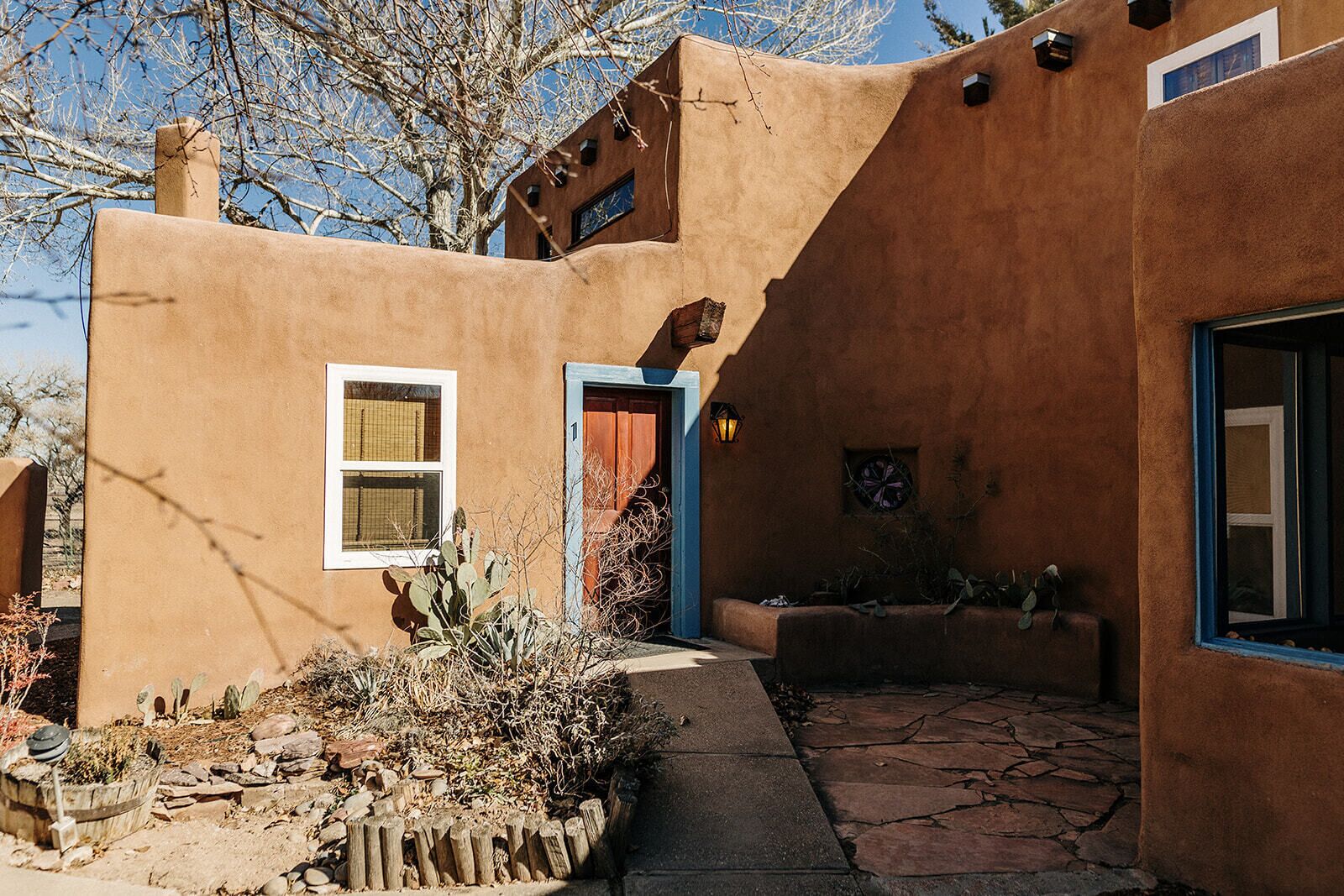 A stucco building with a blue door and windows, a stone pathway, and desert vegetation.